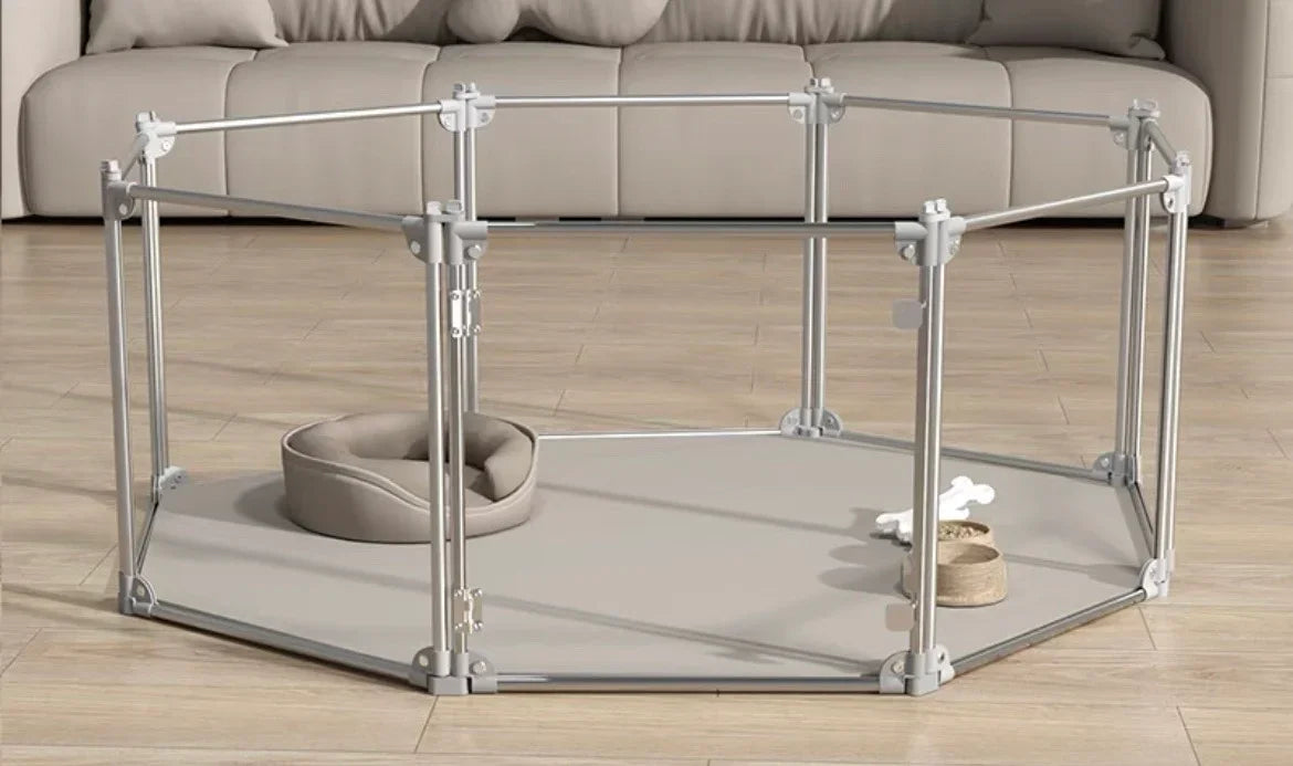 Indoor metal pet playpen with beige bed, bowl, and toy on wood floor in front of sofa